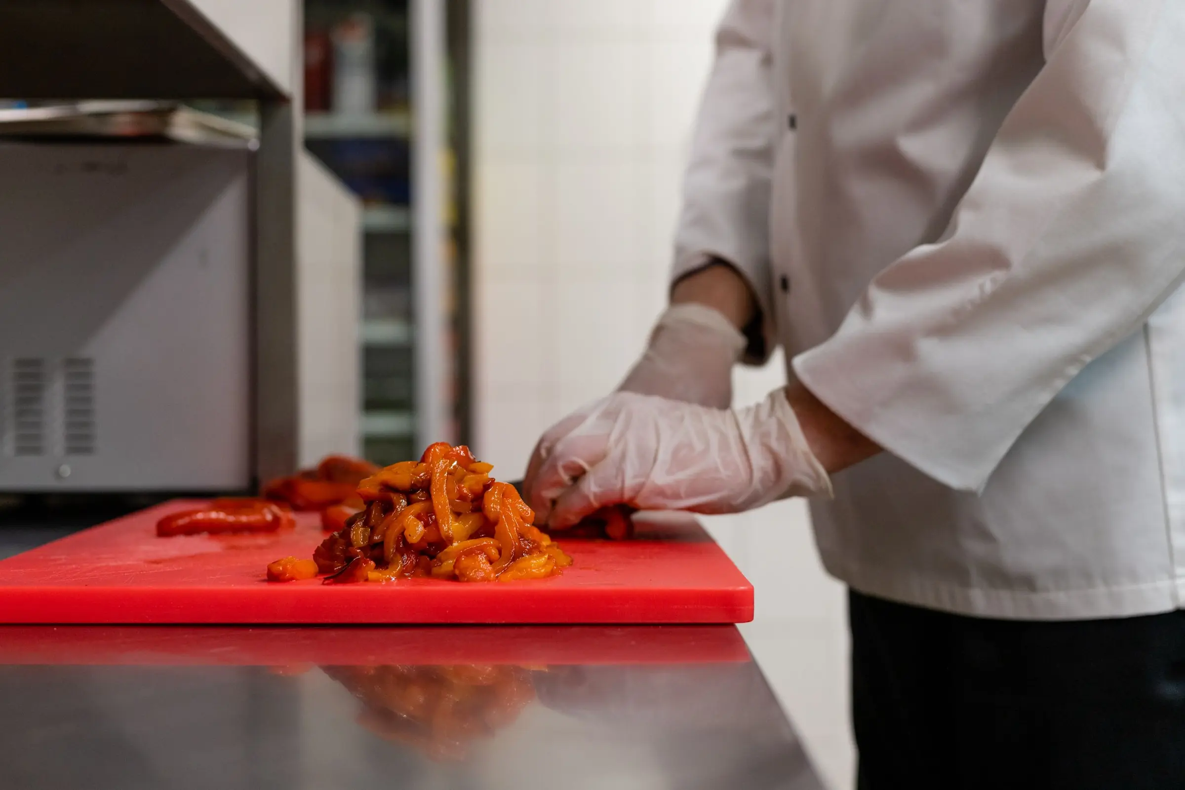 Koch schneidet gegrillte Paprika auf einem roten Brett